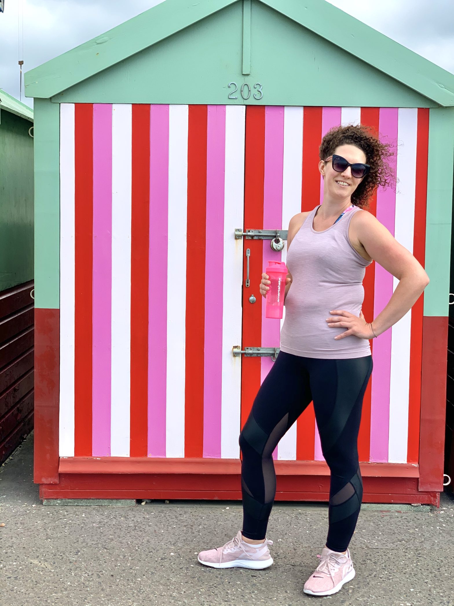 Becky Hughes, personal trainer, poses in front of a pink stripy beach hut