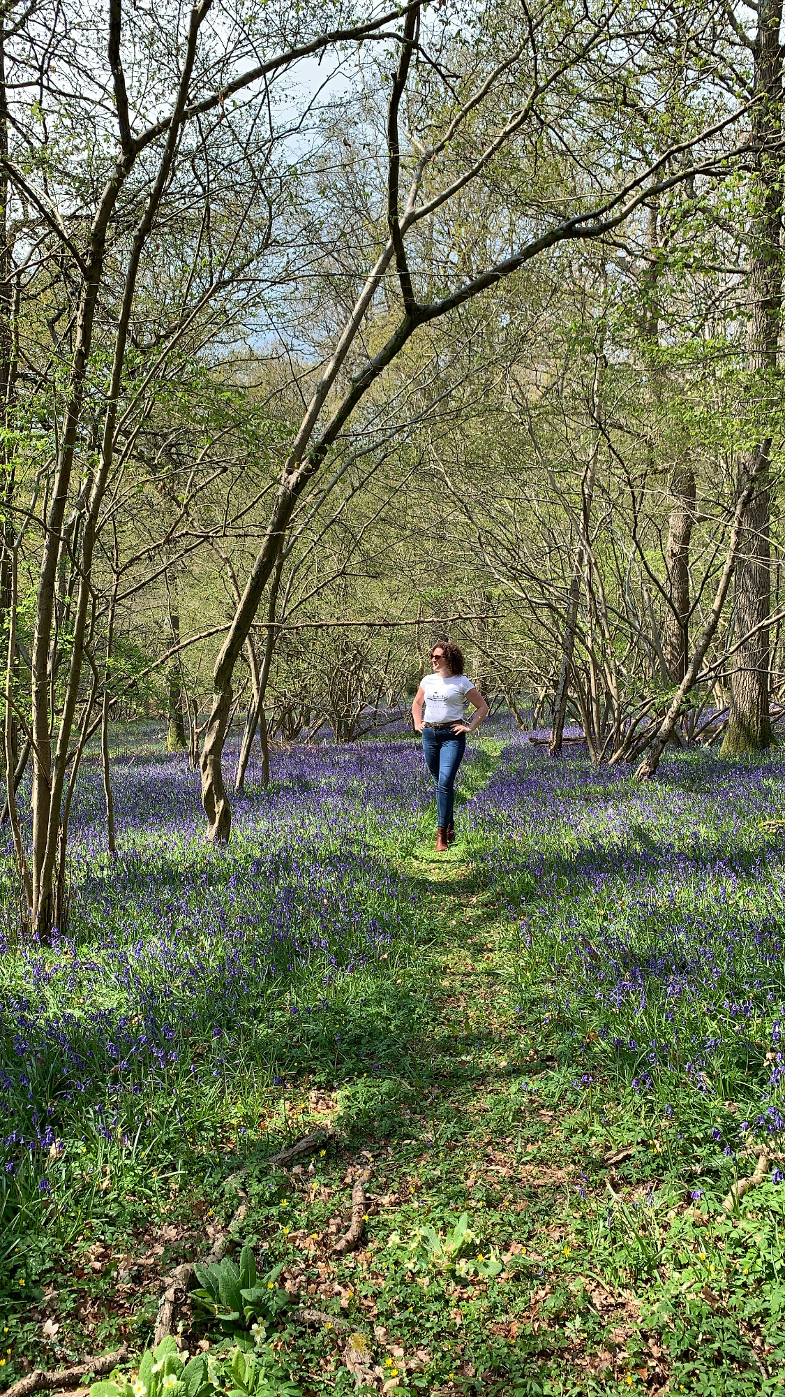 Becky Hughes walks through a wooded area, the ground is covered in bluebells