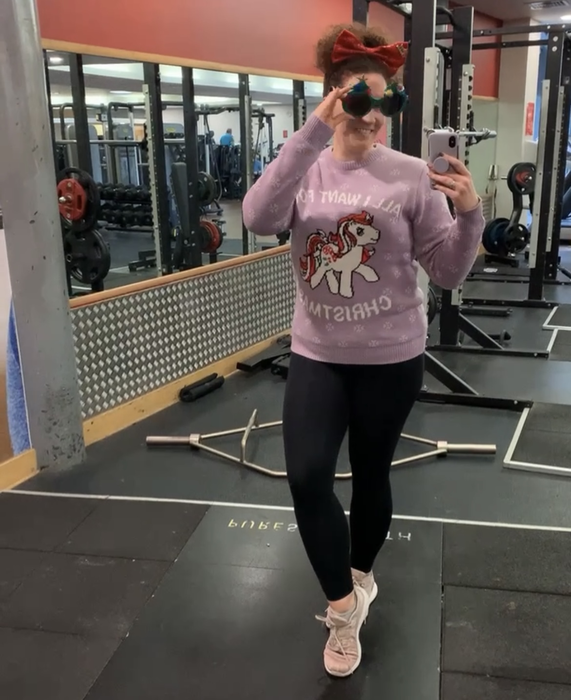 Becky Hughes, personal trainer, stands in a gym wearing a Christmas jumper and festive glasses