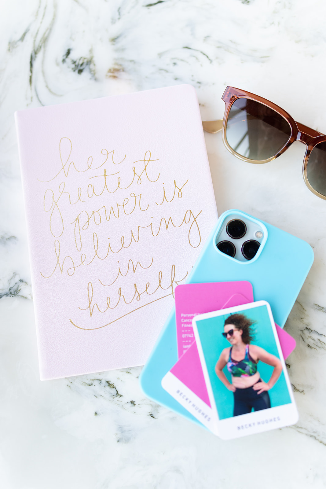 Items on a table, a notepad reads 'Her greatest power is believing in herself' near the business cards of personal trainer Becky Hughes