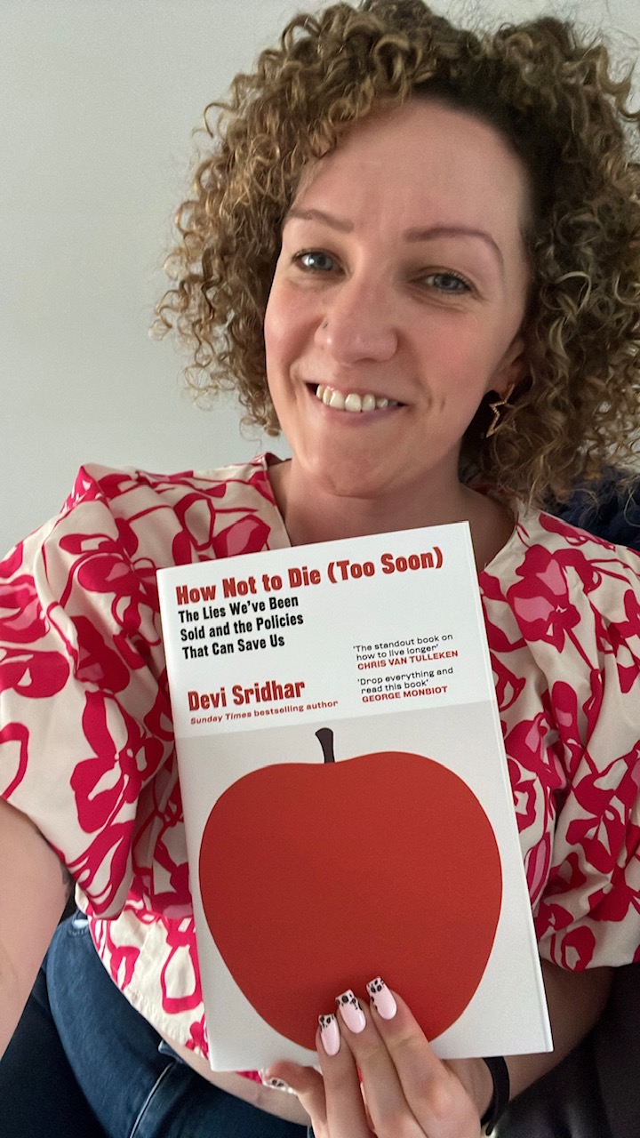 Selfie of Becky holding a copy of How Not to Die (Too Soon), she is smiling