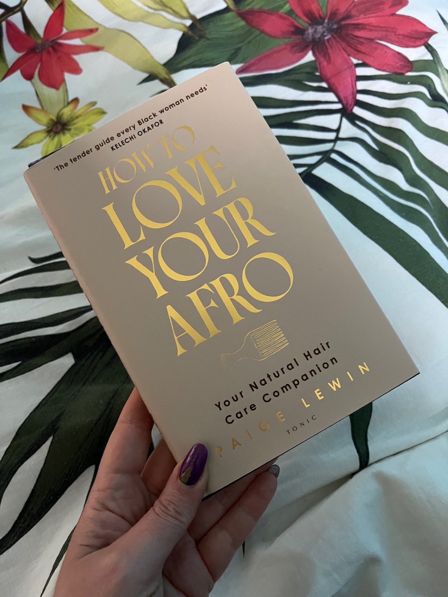 White manicured hand holds a copy of How to LoveYour Afro