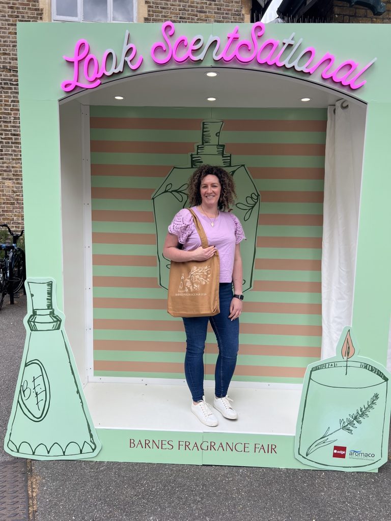 Becky, a White woman, stands inside a brand box frame at Barnes Fragrance Fair