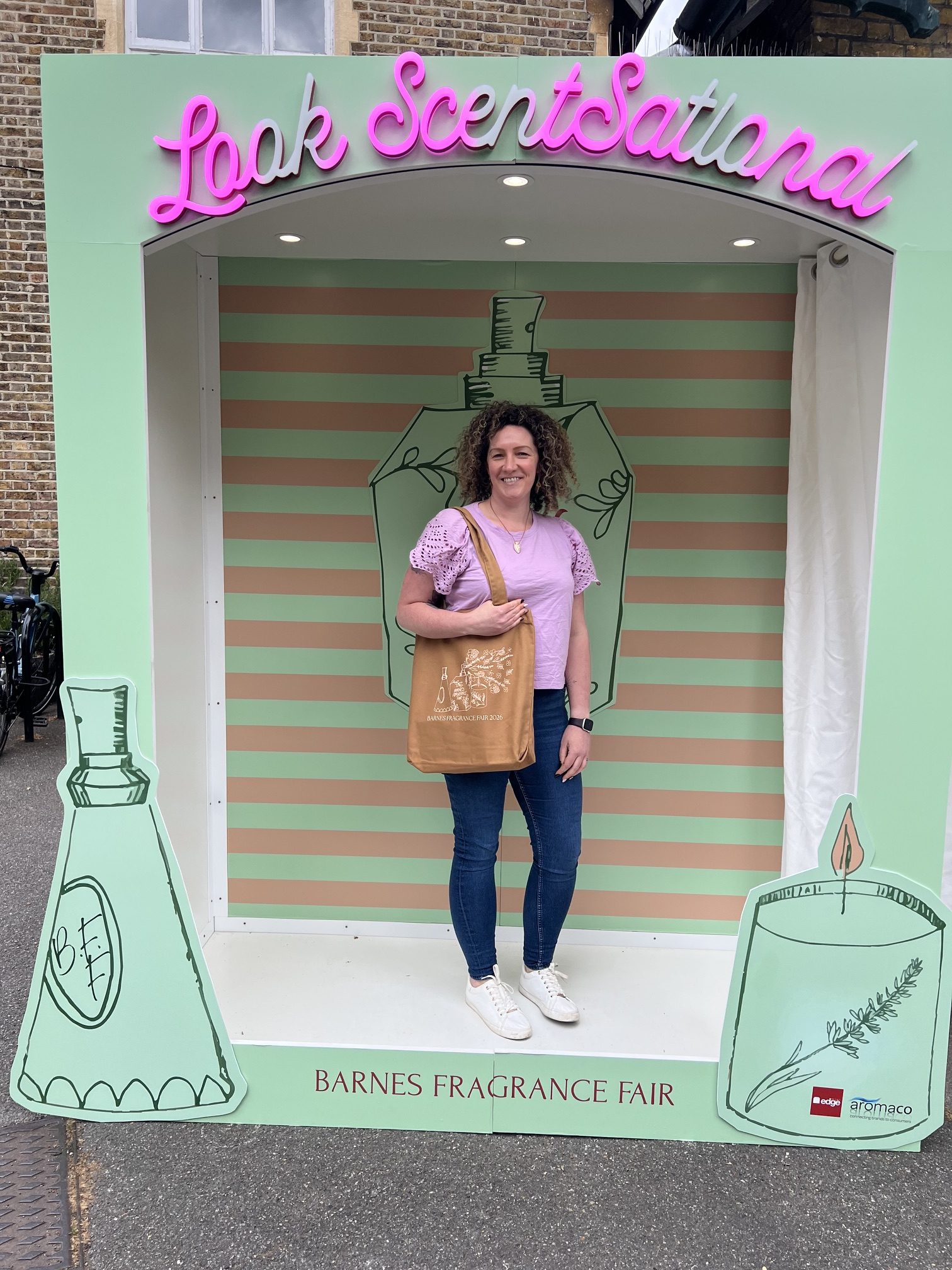 Becky, a White woman, stands inside a brand box frame at Barnes Fragrance Fair